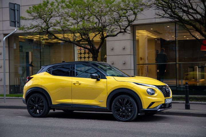Żółty Nissan Juke stojący bokiem na tle budynku i drzew