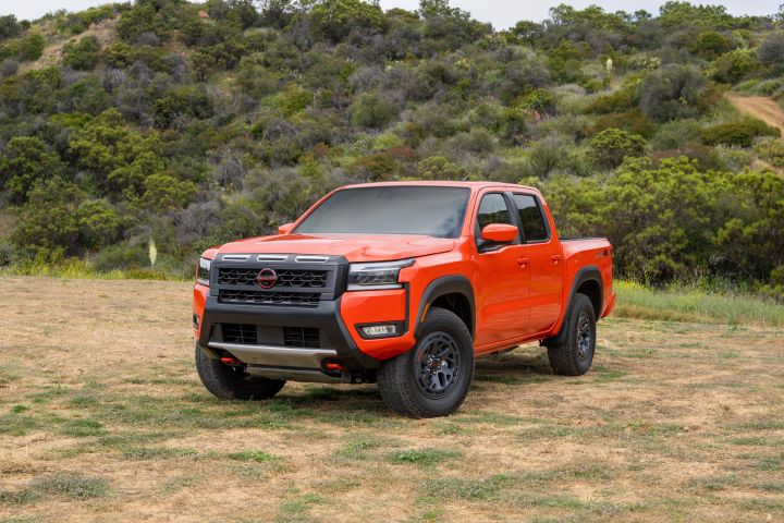 Left 3/4 view of the 2026 Nissan Frontier PRO-4X parked in a grassy area with trees behind.