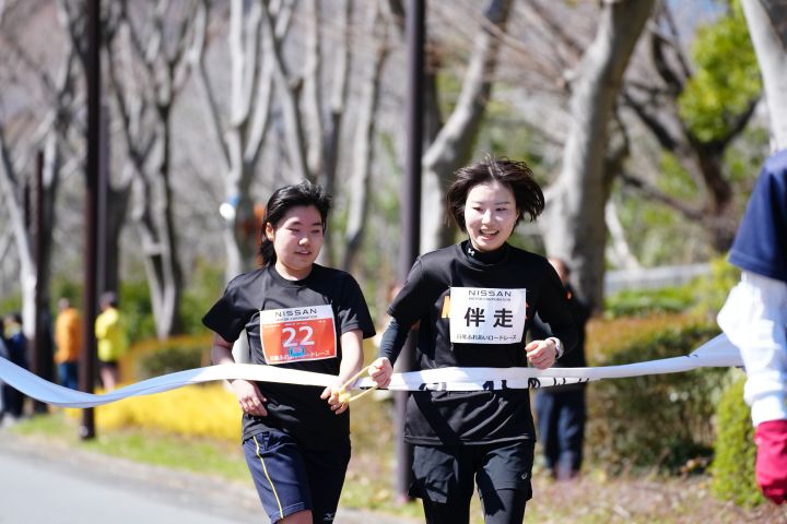 黒いTシャツを身に着けた女性の選手と同じく黒いTシャツを身に着けた伴走者が笑顔でゴールする様子
