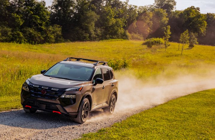 Front left 3/4 view of a 2025 Nissan Rogue rock creek driving on a dirt road with dust billowing behind from speed.