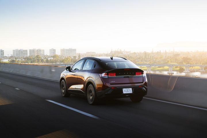 Angled rear view of the 2026 Nissan LEAF driving along a city highway.