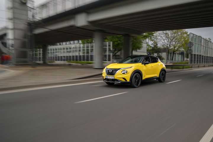 Jadący żółty Nissan Juke (widok z półprofilu) z budynkami w tle