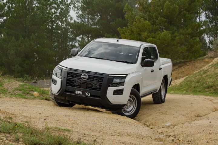 2026 Nissan Navara SL dual cab ute finished in Alpine White captured from the front-right on uneven gravel, highlighting suspension travel, steel wheels and black grille detailing.