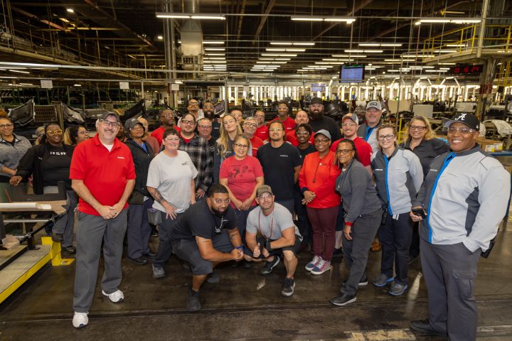 Brie Larson and a large crowd of Nissan workers pose for a group photo in a manufacturing plant.