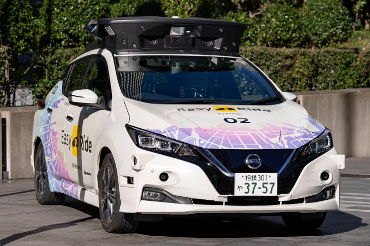 На цьому фото зображено білий автомобіль Nissan на фоні зелених дерев
