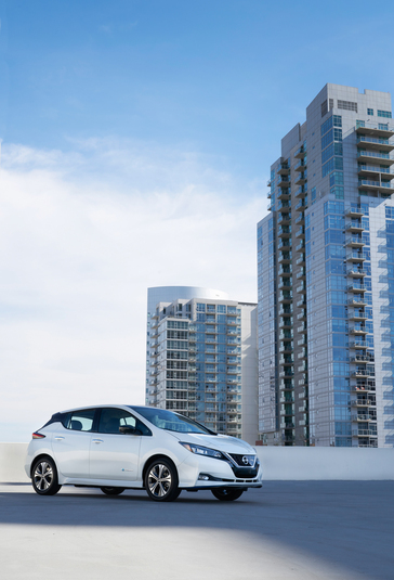 A white 2019 Nissan LEAF PLUS on top of a parking structure with a building in the background