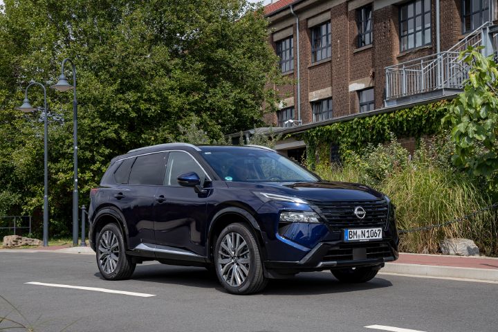 Blick von schräg vorne auf einen dunkelblauen Nissan, der auf einer Straße vor einem begrünten Backsteingebäude steht