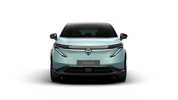 A light blue vehicle is photographed from a front diagonal angle, emphasizing its aerodynamic design and modern appearance. The background is an outdoor exhibition event.