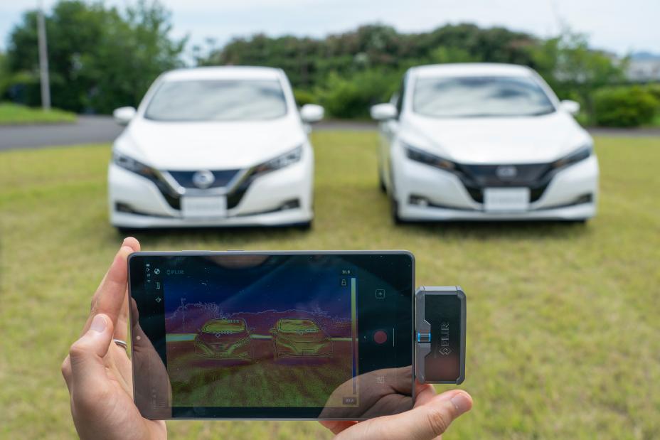 Nebeneinander in der Sonne geparkt, zeigt die Spezialausrüstung im Vordergrund den Unterschied in der Oberflächentemperatur eines Fahrzeugs mit der Cool-Painting-Technologie von Nissan im Vergleich zu herkömmlichen Lacken