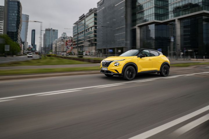Jadący żółty Nissan Juke (widok z boku) z budynkami w tle