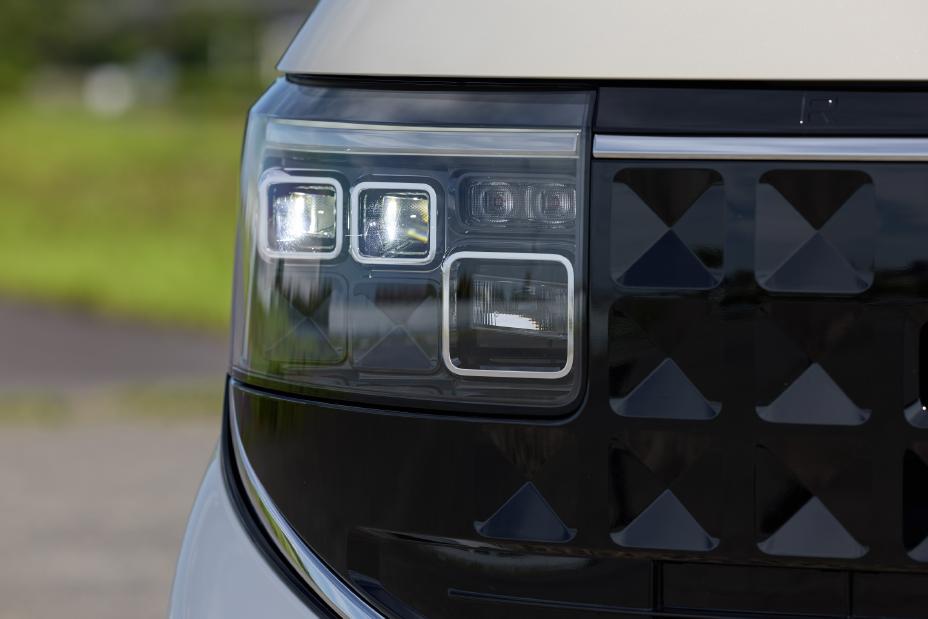 A close-up of the square-shaped LED headlight of the new Nissan Roox kei car. The background features a blurred green area.