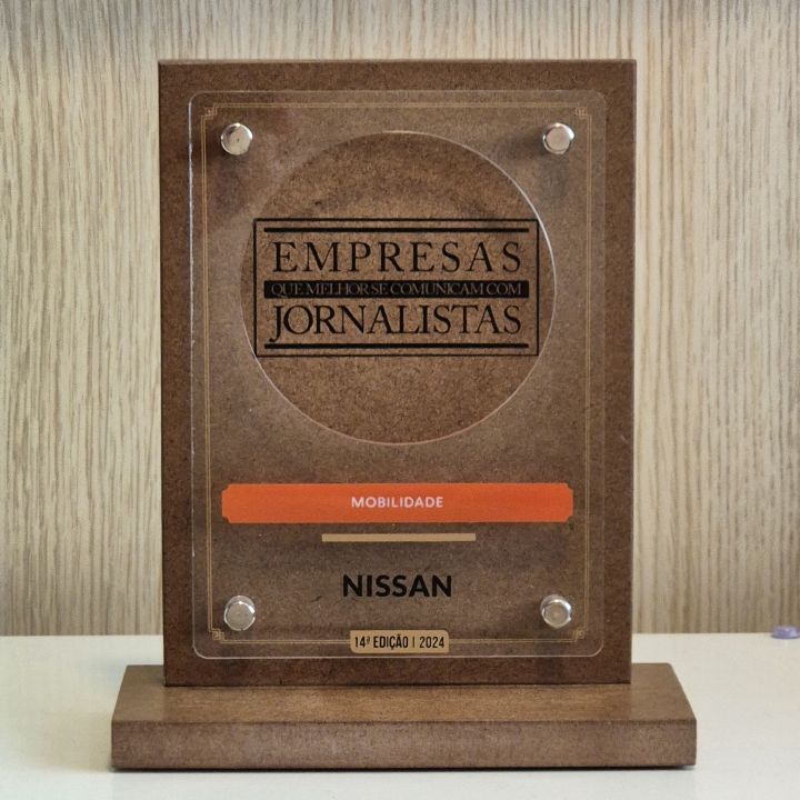 Troféu do prêmio com os dizeres gravados em destaque ‘’Empresas que melhor se comunicam com jornalistas’’, abaixo em destaque laranja escrito ‘’Mobilidade’’, o logo da Nissan e os dizeres gravados em fonte pequena ‘’Décima quarta edição dois mil e vinte e quatro’’