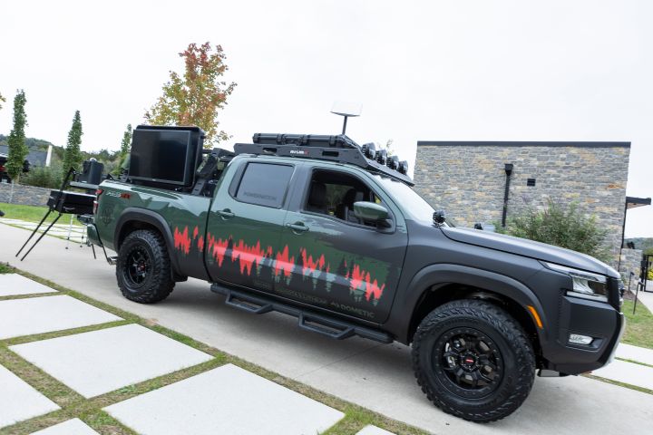 A 2025 Nissan Frontier Trailgater edition parked on cement tiles, it is green with a TV mounted on the truck bed.