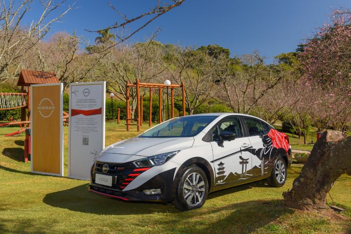 Carro branco com a pintura de um samurai na lateral e detalhes em vermelho, ao lado de dois totens da Nissan e, ao fundo, a cerejeira