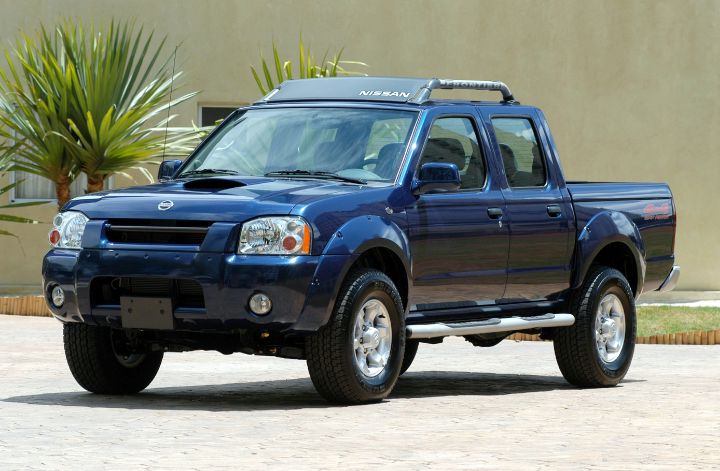 Nissan Frontier 2002 na cor azul sobre chão de pedras com árvores ao fundo