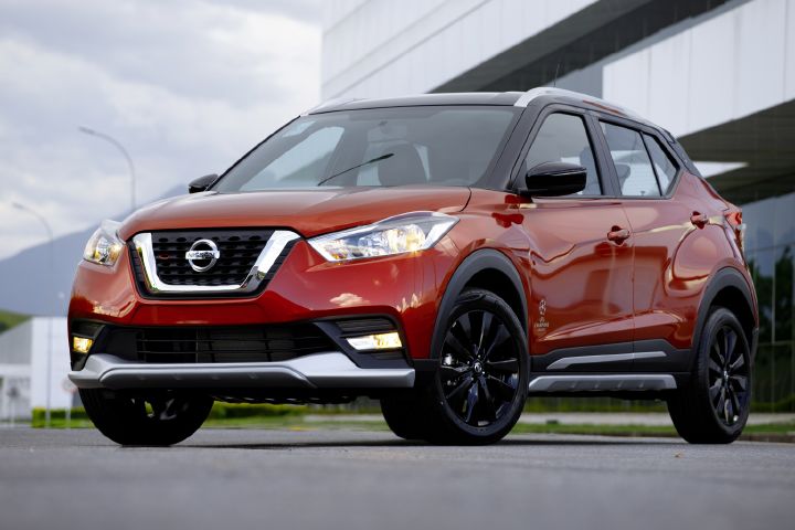 Kicks UEFA vermelho de ¾ de frente em frente ao escritório da fábrica da Nissan