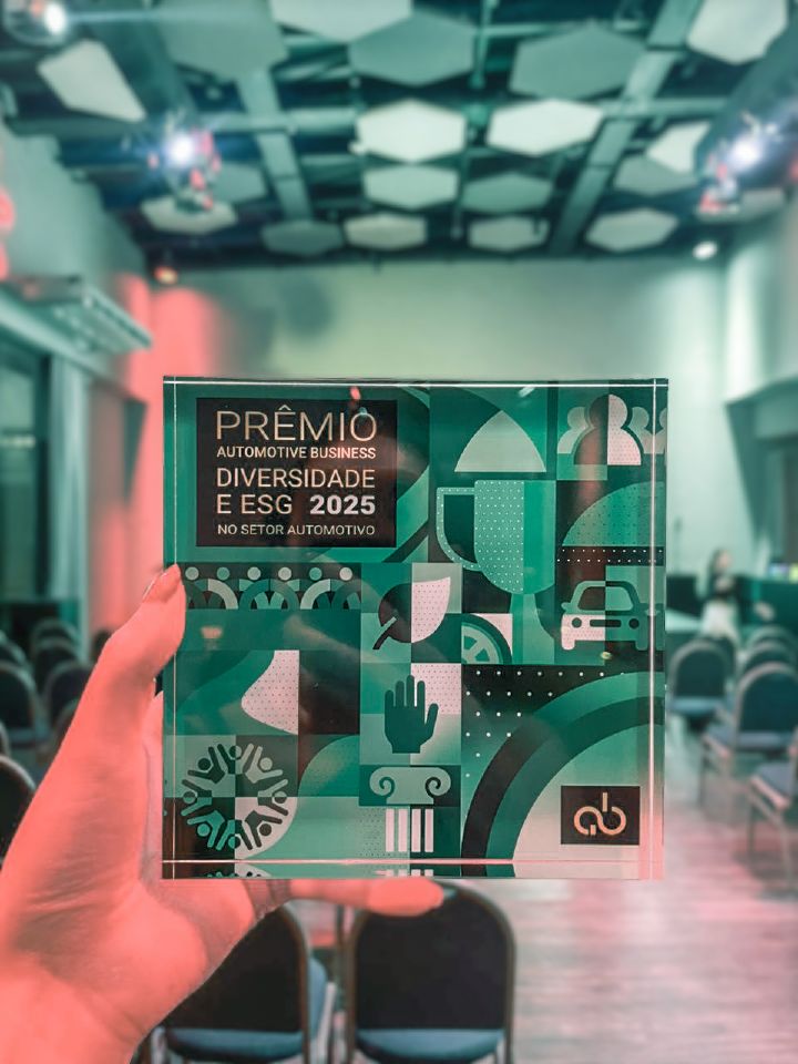 Mão segura um troféu com a mensagem “PRÊMIO AUTOMOTIVE BUSINESS DIVERSIDADE E ESG 2025 DO SETOR AUTOMOTIVO”