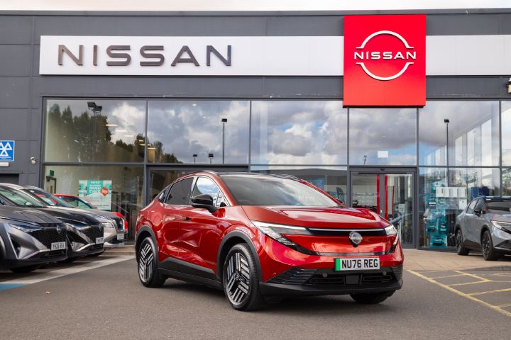 Red Nissan LEAF shown from a three-quarter angle parked in front of a Nissan dealership.