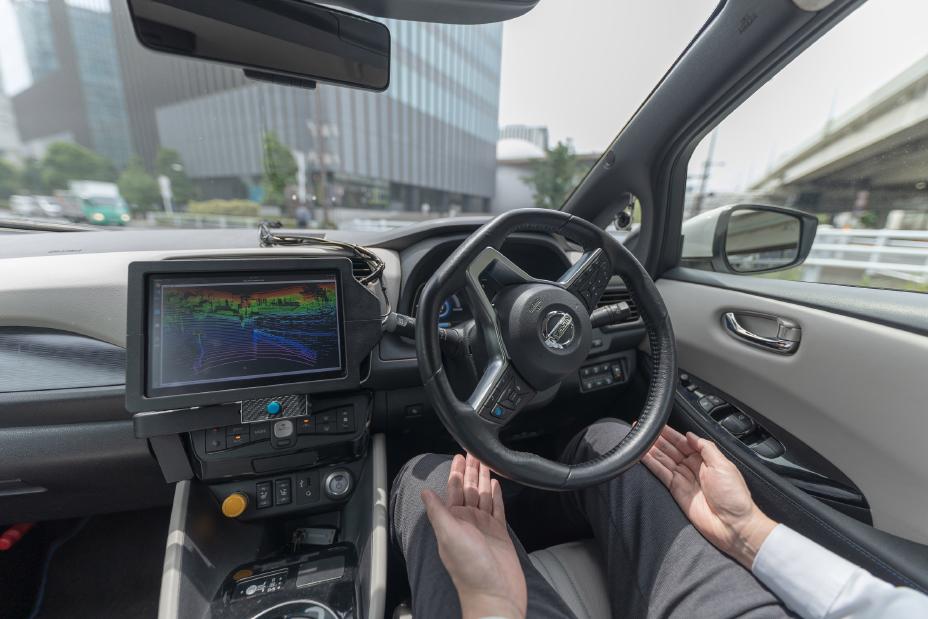 Bestuurder rijdt met zijn handen los van het stuur; in het midden de monitor in de Nissan LEAF-testauto van Easy Ride