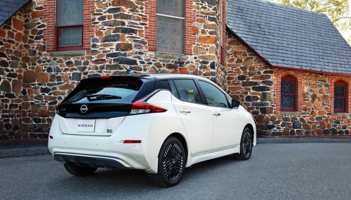 Right rear 3/4 view of a white 2025 Nissan LEAF parked in front of a warm-toned stone building.