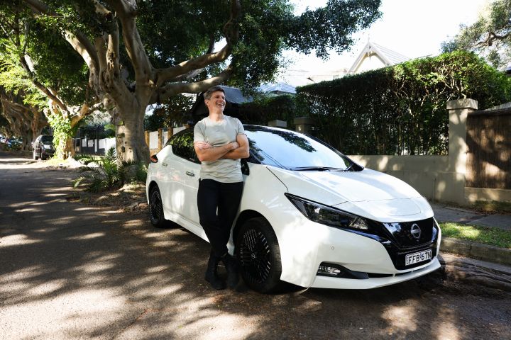 Nissan Australia ambassador Osher Gunsberg stands next to his white Nissan LEAF that is parked on a street