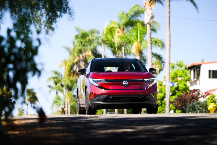 Front view of the 2026 Nissan LEAF driving on a road near palm trees.