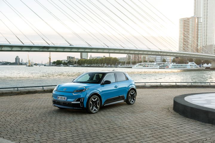 Ein blauer Nissan Micra steht schräg im Abendlicht auf einem asphaltierten Platz vor Wasser und Brücke in Rotterdam