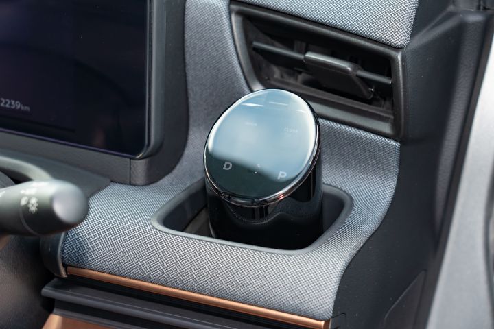 Interior of a Nissan SAKURA showing a black circular solar meter on the center console. Surrounding materials are gray fabric with metallic accents, with part of a display on the left and an air vent on the right.