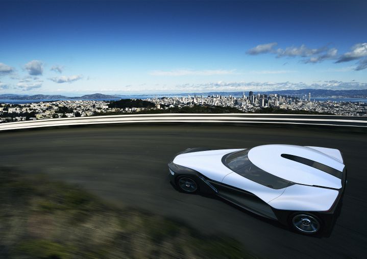 A white car driving down a road with a city in the background.