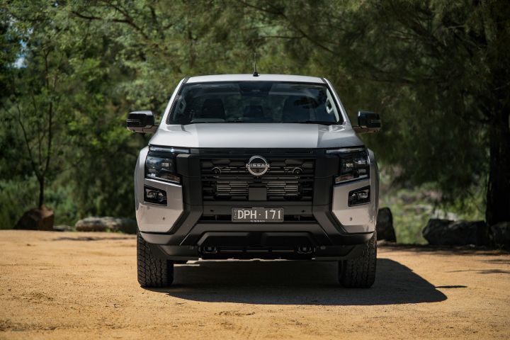 2026 Nissan Navara ST dual cab ute finished in Summit Silver shown head-on on a sandy clearing, with the black grille, upright stance and wooded backdrop.