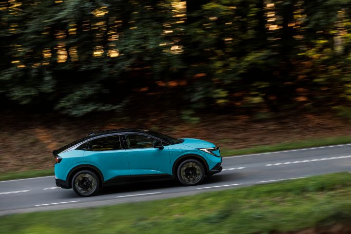 Seitliche Fahraufnahme eines türkisen Nissan LEAF vor einem dunklen Waldstück