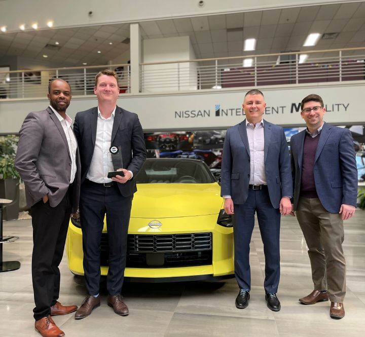 Nissan employees posing for a picture next to a Nissan vehicle