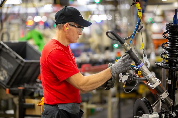 A man in a red Nissan shirt working with machines on a Nissan manufacturing plant floor.