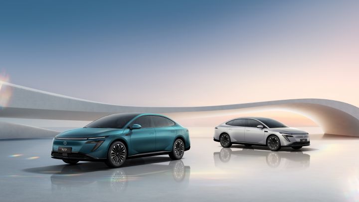 東風日産の緑色の新型セダン電気自動車「N7」2台。左は緑色、右は白、日の出を背景にうねる建築物が見える
