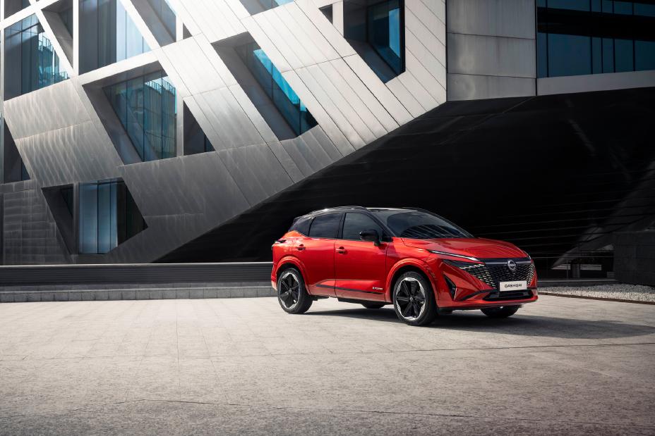 Nissan Qashqai rouge Fuji de ¾ avant droit garé devant un bâtiment moderne