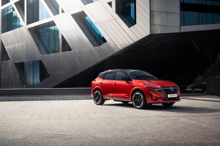 Nissan Qashqai rouge Fuji de ¾ avant droit garé devant un bâtiment moderne