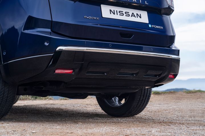 Neuer 2026 Nissan X‑Trail Tekna in der Außenfarbe Universal Blue, hinterer unterer Teil auf unbefestigtem Untergrund mit sichtbaren Reifen und Fahrwerk. Das Nummernschild trägt das Nissan-Logo sowie die Aufschriften „e‑POWER” und „e‑4ORCE”, die auf die Hybrid- bzw. Elektroantriebstechnologie hinweisen.
