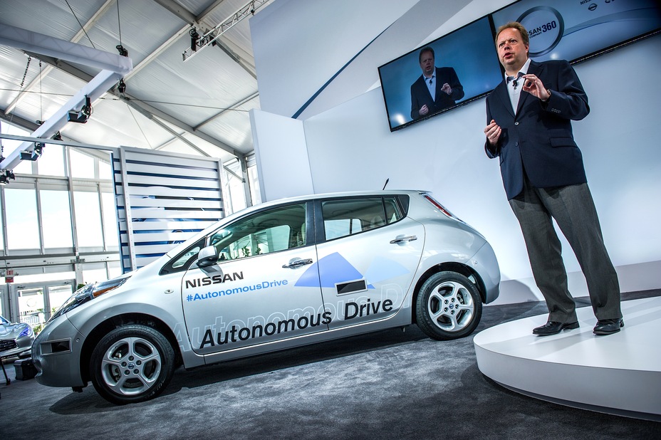 a man giving a speech in a platform next to a silver Nissan vehicle