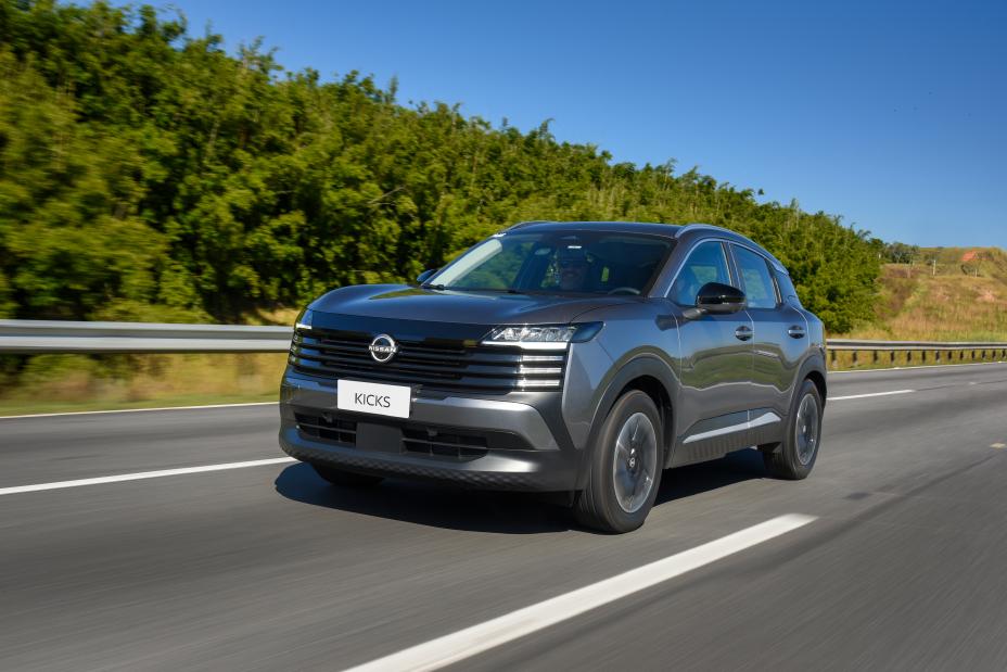 Modelo Advance do Novo Nissan Kicks de cor cinza, andando em alta velocidade em uma rua asfaltada com árvores ao fundo de paisagem
