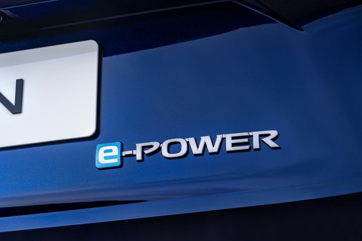 Neuer 2026 Nissan X‑Trail Tekna in der Außenfarbe Universal Blue mit einem metallischen „e‑POWER”-Emblem mit dem Buchstaben „e” in einem blauen Quadrat am Heck. Das Bild hebt das Branding im Zusammenhang mit der Hybridantriebstechnologie des Fahrzeugs hervor.