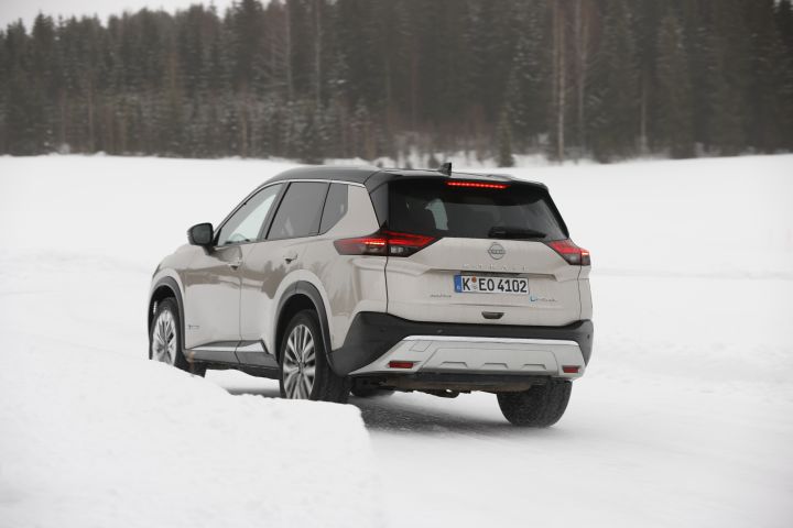 Fahraufnahme 3/4 Heck eines silbernen Nissan X‑Trail e‑Power e‑4ORCE in verschneiter Landschaft