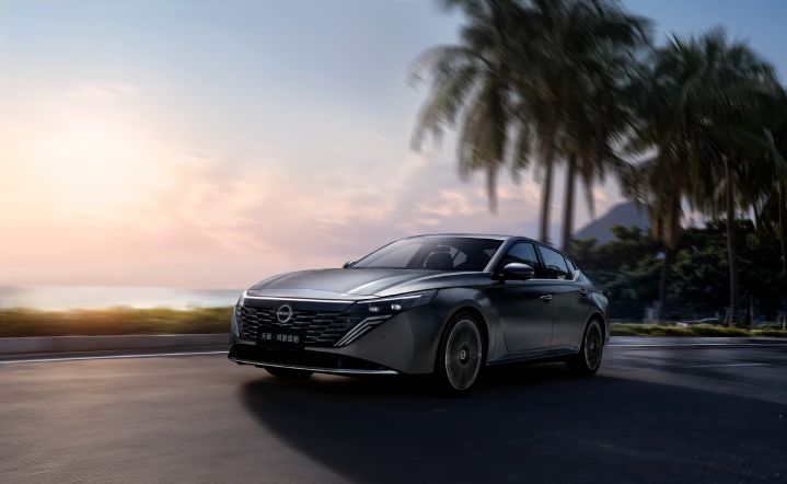 A black Teana driving along a coastal road. The car is facing right, showing its front and side. The background features palm trees, the ocean, and distant mountains, with soft sunlight from either sunrise or sunset.