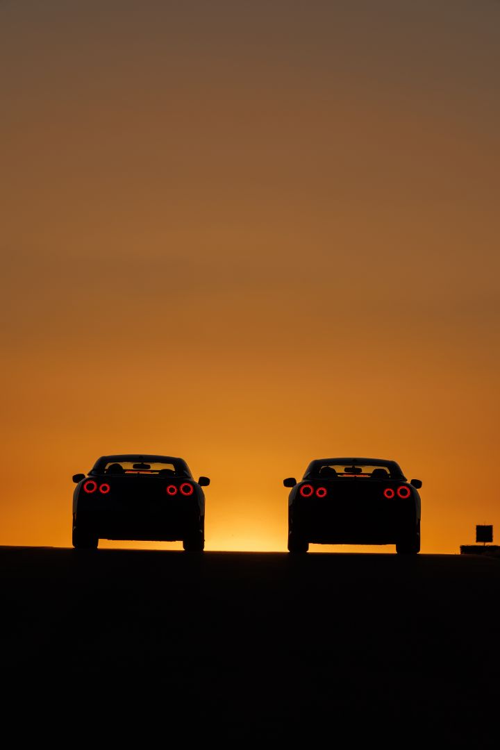 Silhouette of two special edition Nissan GT‑R rear ends with a dark foreground and sunset in background