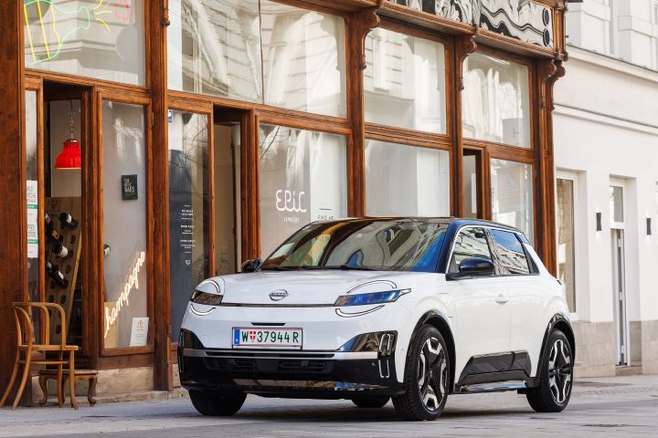 3/4 Frontansicht eines weißen Nissan Micra mit schwarzem Kontrastdach, der vor einem Café mit großen Fenstern mit Holzrahmen parkt