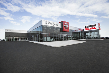 Bâtiment moderne de concession automobile Nissan avec une grande façade vitrée et une signalétique Nissan bien visible sous un ciel clair.