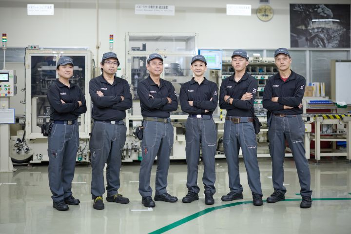 Six Nissan employees standing together in dark uniforms with their arms crossed.