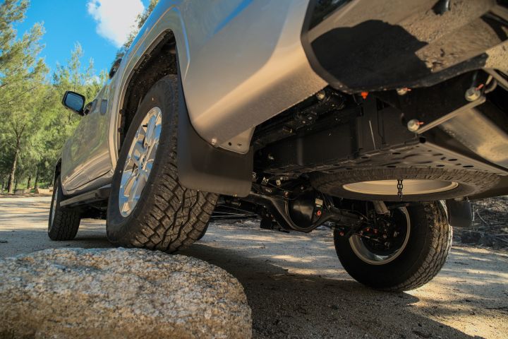 2026 Nissan Navara ST dual cab ute finished in Summit Silver viewed from a low underside angle, showing the spare wheel, rear axle and off-road clearance over rock.