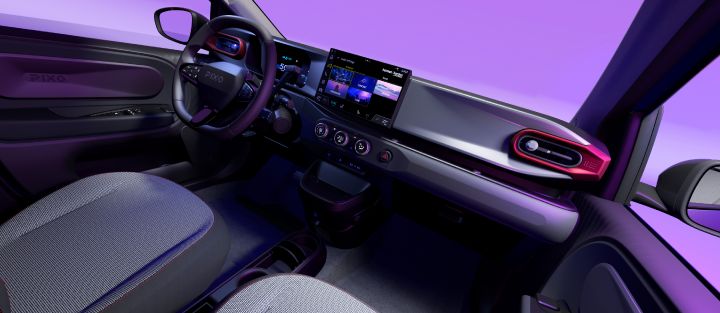 Panoramic view of Nissan PIXO’s interior cabin with steering wheel, digital instrument cluster, central touchscreen, climate controls, and textured seats. Red-accented air vents, black dashboard trim, compact center console