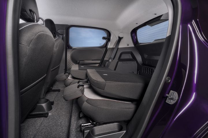 Das Foto zeigt den hinteren Fahrgastraum eines Kleinwagens mit grauer Polsterung, violettem Türrahmen, getönten Scheiben und schwarzem Teppichboden. Die geteilt umklappbaren Rücksitze sind nach vorne geklappt, wodurch die flexible Sitzanordnung und das vergrößerte Kofferraumvolumen deutlich werden.