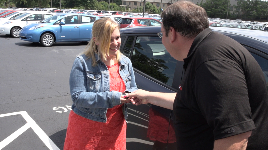 a man giving a key to a woman next to a vehicle